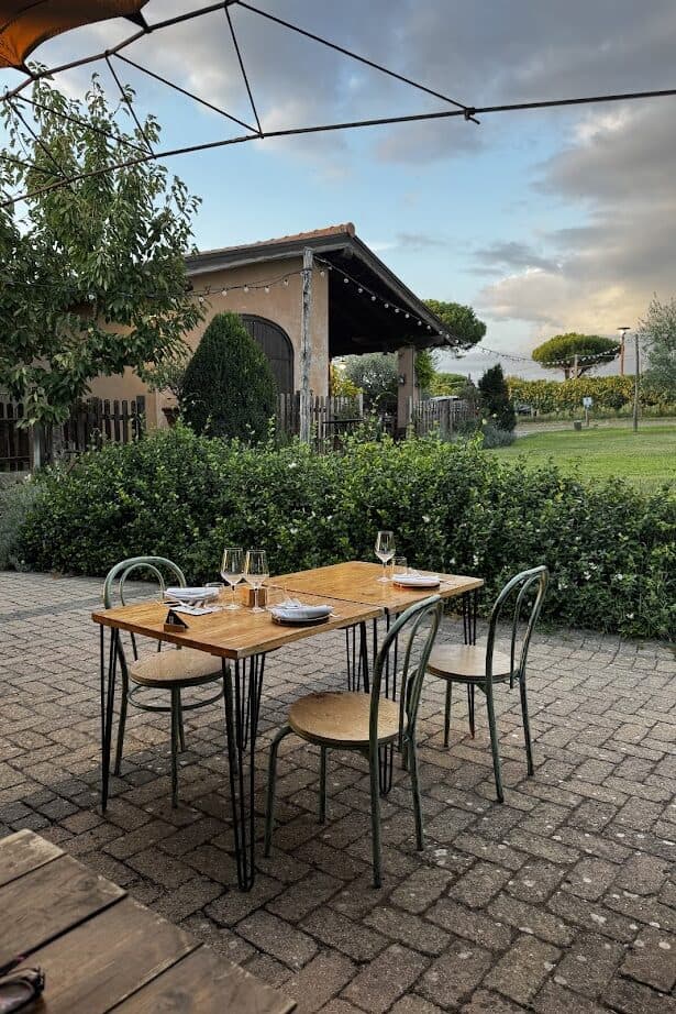 A set table for four on a patio overlooks a garden and rustic building under a partly cloudy sky, evoking the charm of spending 4 days in Castel Gandolfo.