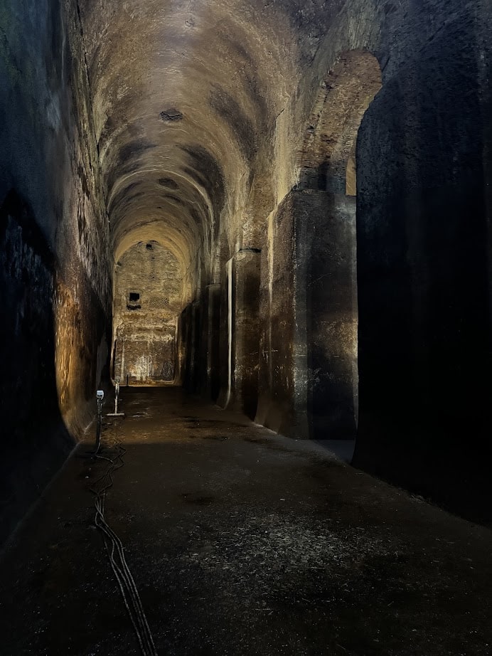 A dimly lit underground vaulted tunnel with arched ceilings and rough stone walls—perfect for exploring during your 4 days in Castel Gandolfo.