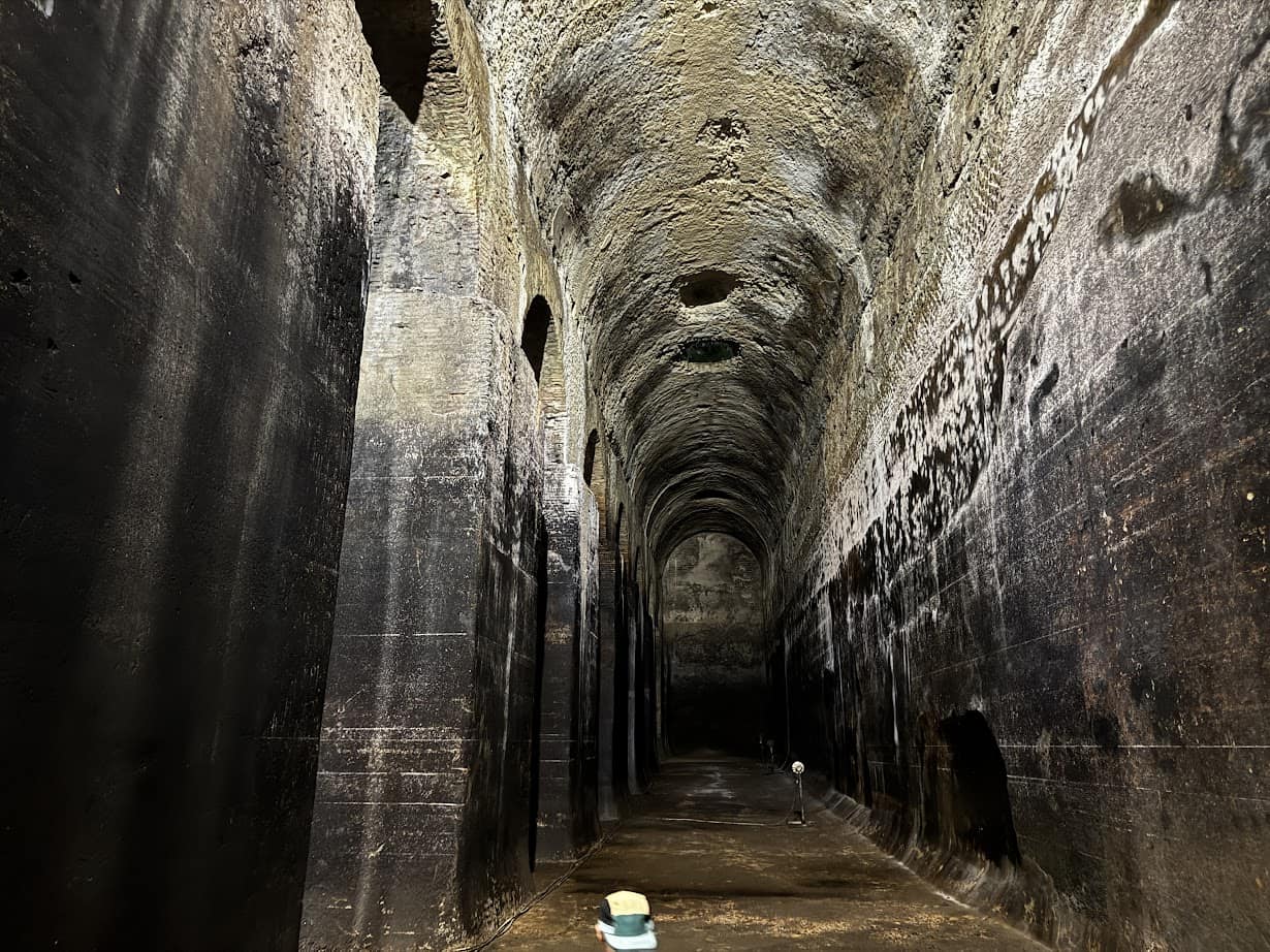 A tall, ancient stone chamber with arched ceilings and dark walls evokes the history felt during 4 days in Castel Gandolfo, while a small cart stands on the wet floor.