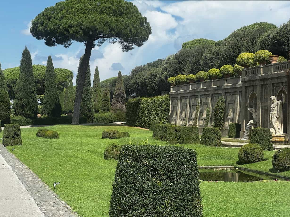 Formal garden with manicured hedges, statues, tall trees, and a decorative stone wall under a blue sky—perfect for spending 4 days in Castel Gandolfo.