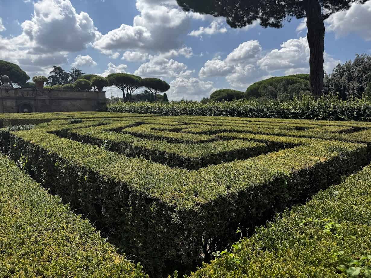 A well-trimmed hedge maze with trees and a partly cloudy sky in the background, reminiscent of the charming gardens you might explore during 4 days in Castel Gandolfo.