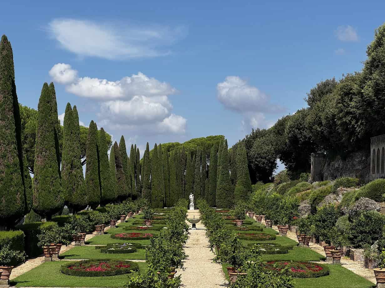A formal garden with tall cypress trees, manicured hedges, and a statue at the end of a central path&mdash;an ideal stop among the best day trips from Rome for families seeking beauty and tranquility.
