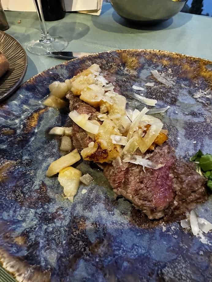 A steak topped with shaved cheese and cooked onions on a blue ceramic plate, perfect after exploring 4 days in Castel Gandolfo.