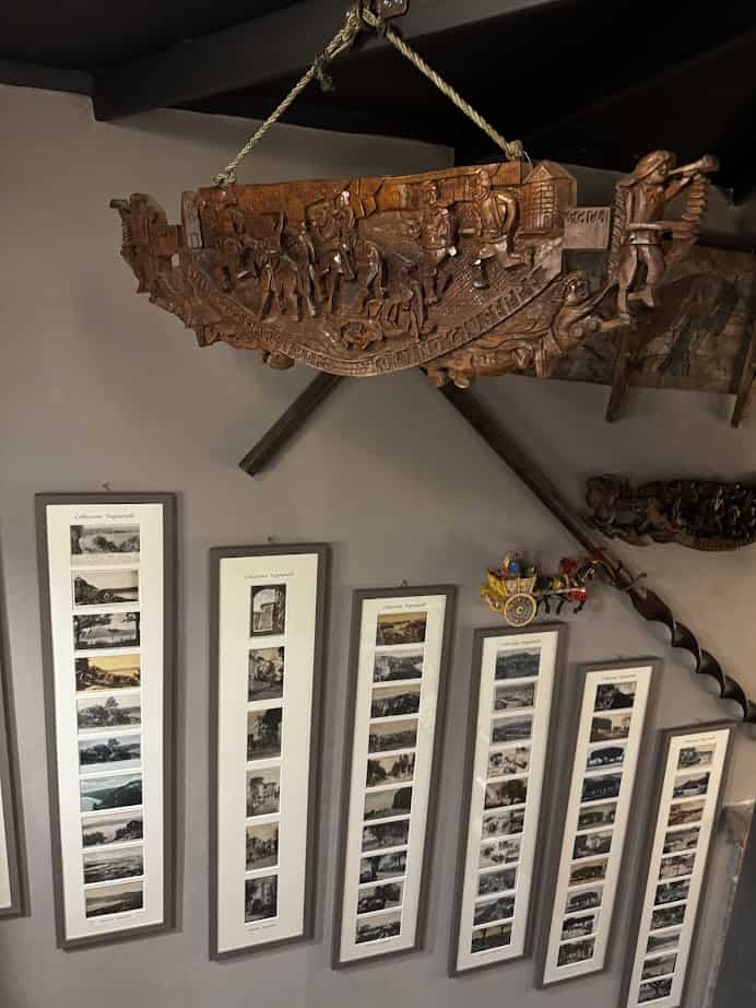 Framed photo collages on a wall beneath a carved wooden decorative piece and a toy horse-drawn carriage capture memories from 4 days in Castel Gandolfo.