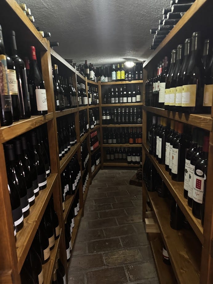 Dimly lit wine cellar with wooden shelves filled with bottles of wine on both sides of a narrow walkway, reminiscent of treasures you might discover during 4 days in Castel Gandolfo.