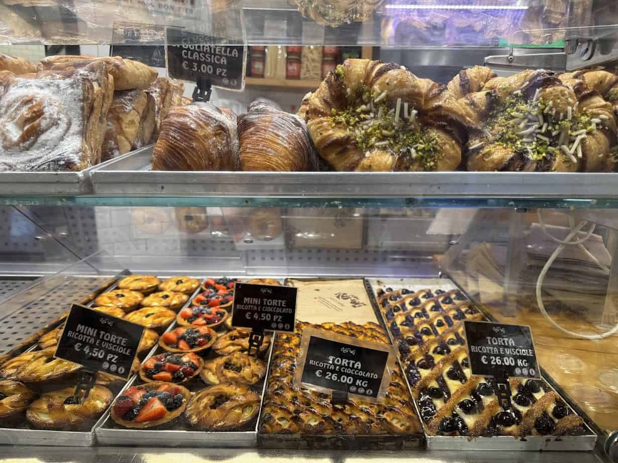 Assorted Italian pastries and cakes, including options found at Gluten Free Restaurants in Rome, displayed in a glass bakery case with price signs in euros.