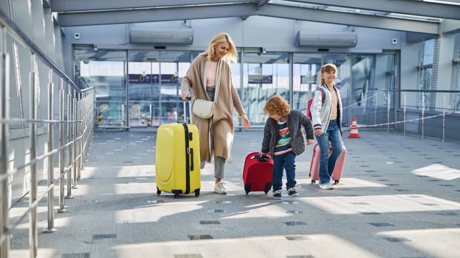 A woman and two children walk through an airport with suitcases, smiling and looking happy.