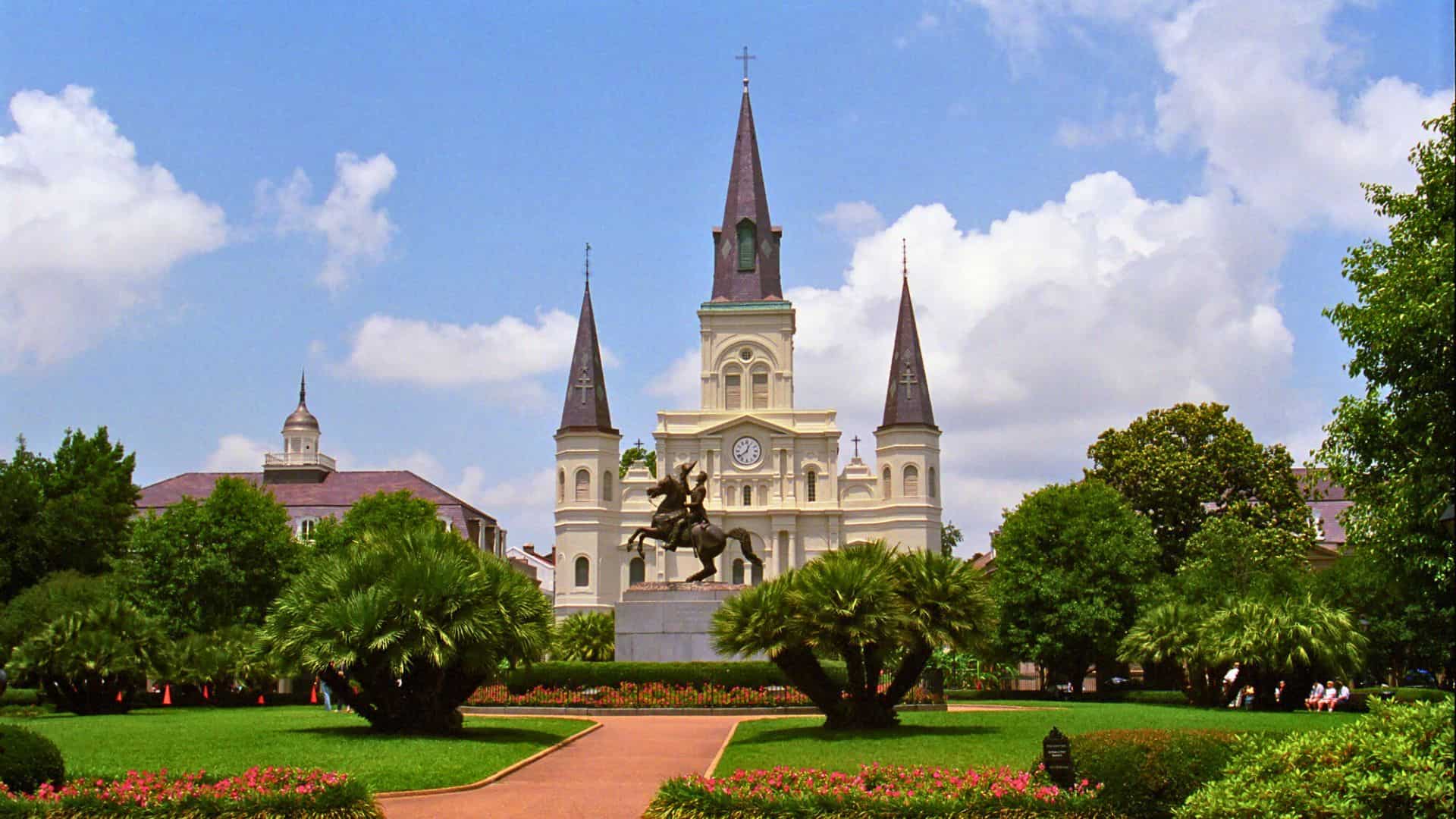 A statue in Jackson Square with St. Louis Cathedral and its three spires in New Orleans under a blue sky.