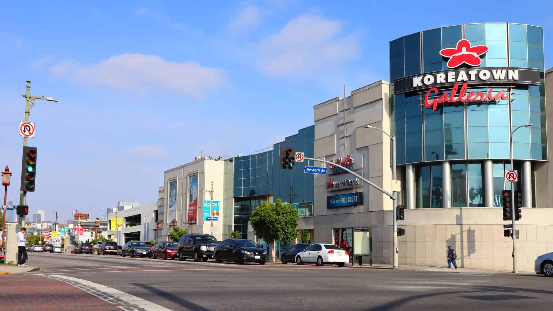 Street view of Koreatown Galleria with cars and pedestrians under a sunny blue sky in Los Angeles.