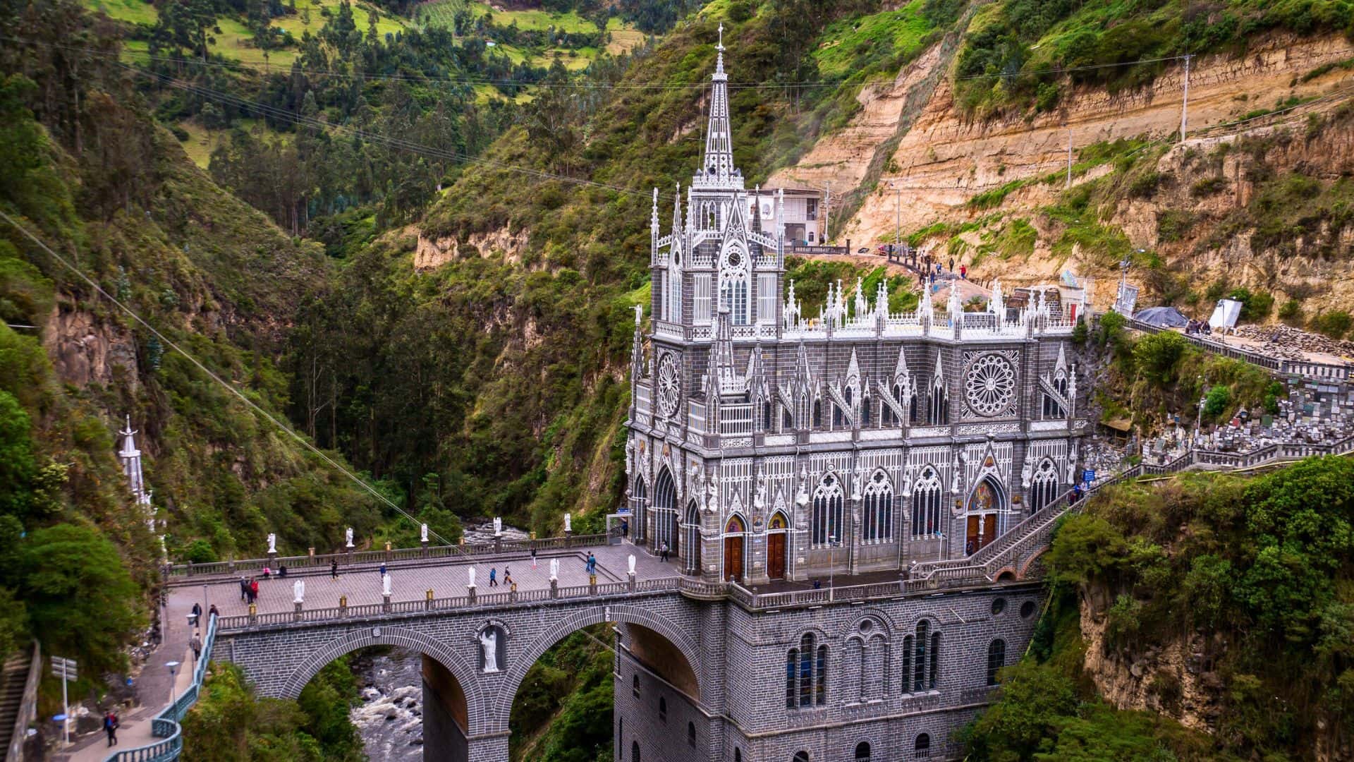 A Gothic-style church spans a gorge, surrounded by lush green hills and a river flowing below.