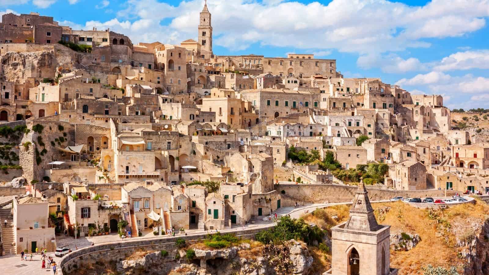 Ancient stone buildings and churches on a hillside under a partly cloudy sky in Matera, Italy.