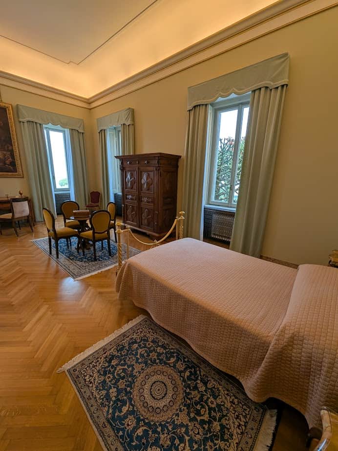 Elegant room with a single bed, round table with chairs, wooden armoire, and large windows with curtains—perfect for relaxing after exploring Castel Gandolfo or unwinding during your 4 days in Castel Gandolfo.