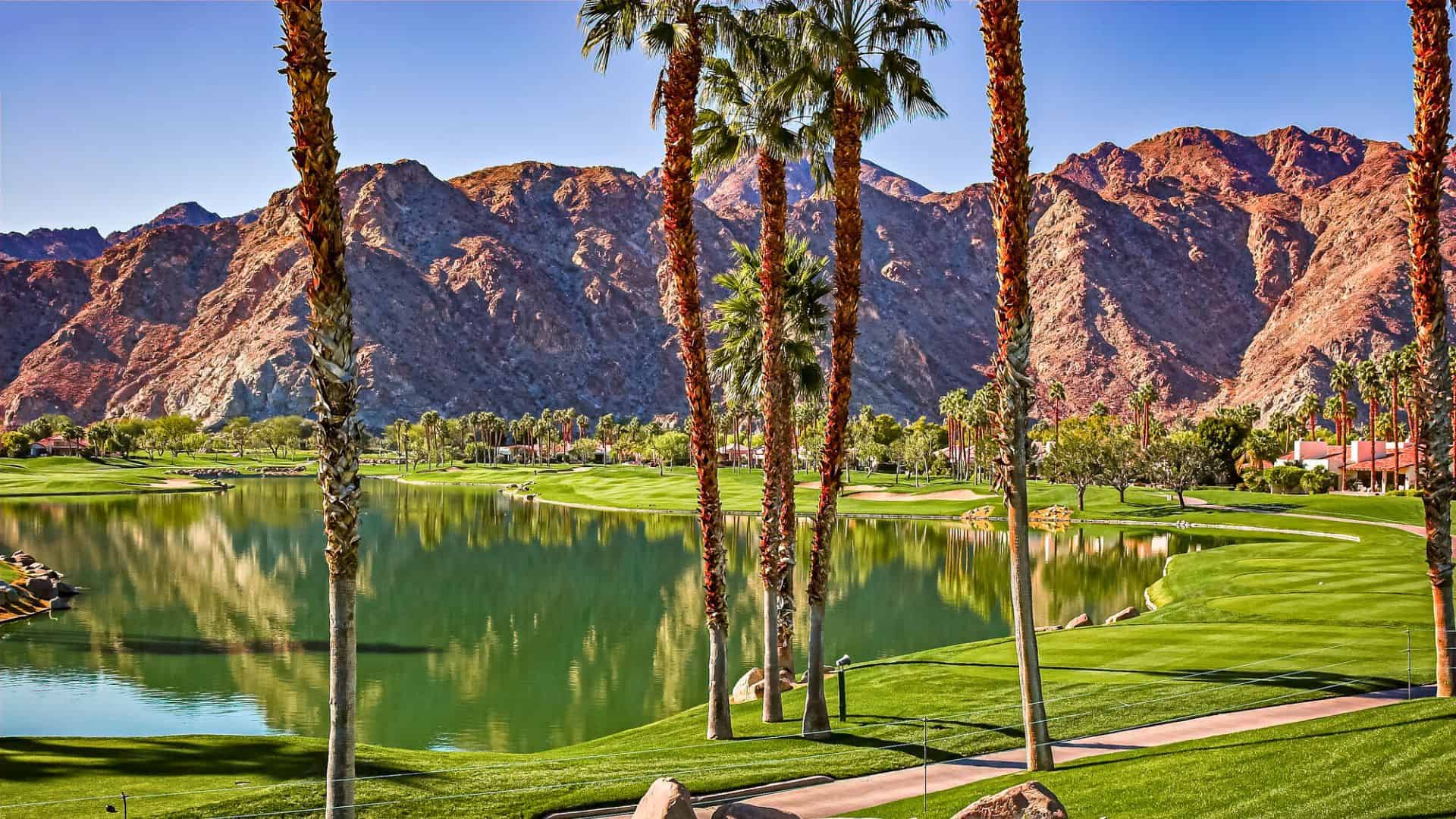 Golf course with palm trees and mountains in the background under a clear blue sky.
