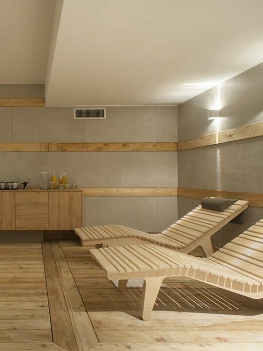 Modern spa room with two wooden lounge chairs, wooden flooring, and a refreshment counter&mdash;echoing the calming ambiance found at the best beach resorts in Italy for families.