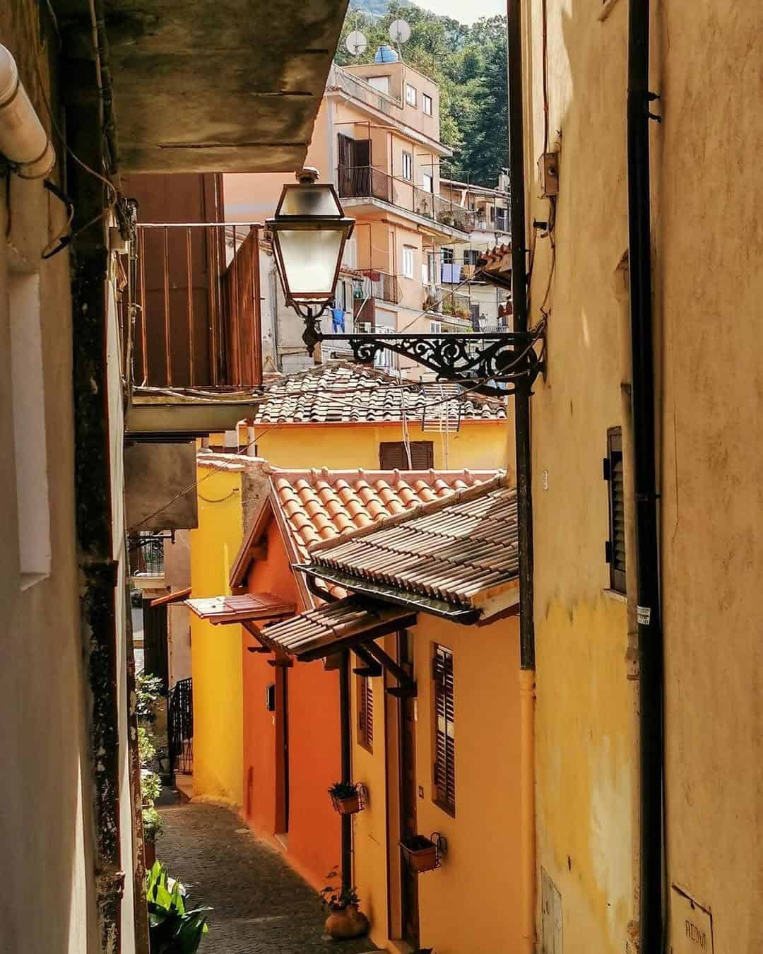 Narrow alley with colorful yellow and orange houses, tile roofs, and a classic street lamp in sunlight—a charming scene you might discover during 4 days in Castel Gandolfo.