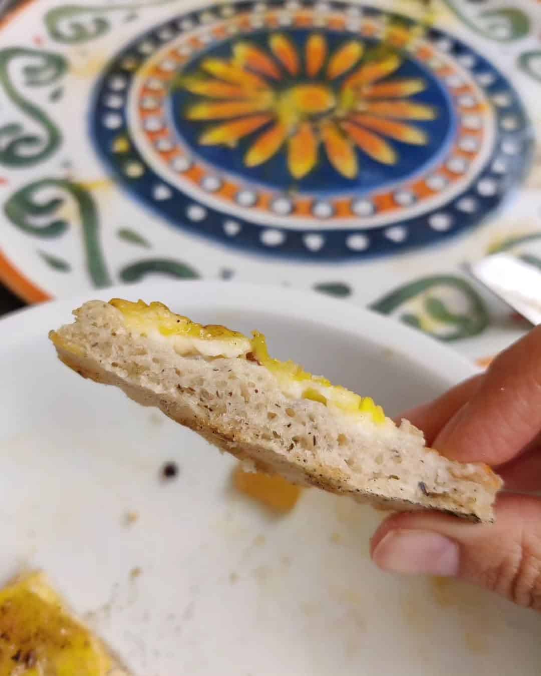Hand holding a piece of bread with melted cheese and egg, colorful plate in the background—a tempting bite you might find at top Gluten Free Restaurants in Rome.