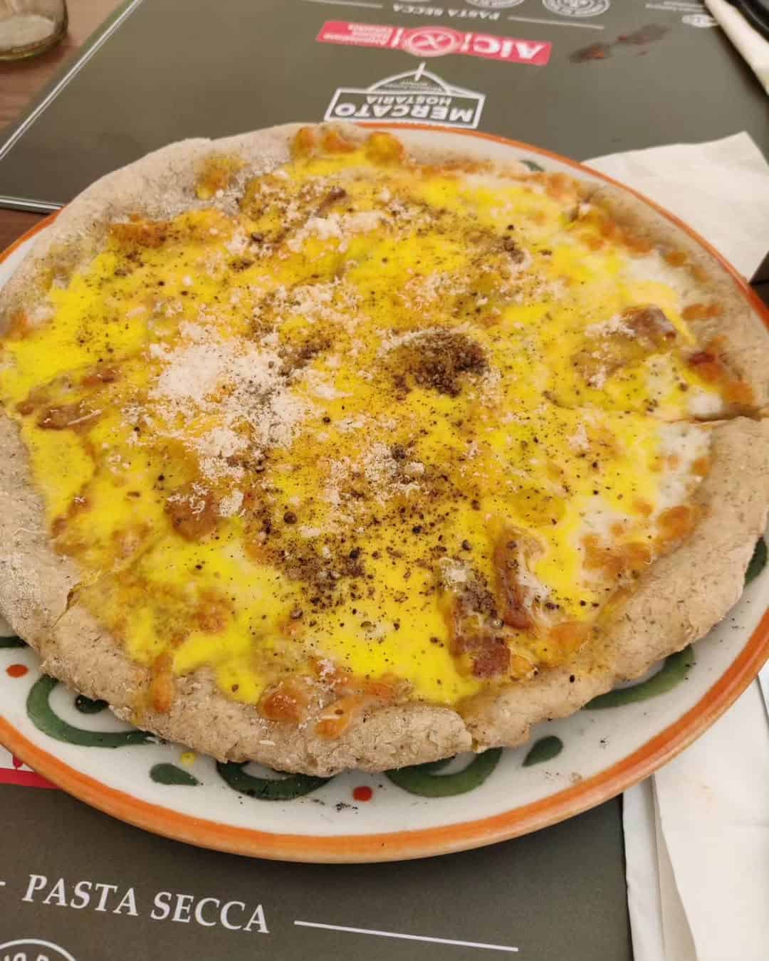 A pizza with a golden yellow topping, cheese, and a sprinkle of black pepper on a decorated plate, perfect for those seeking Gluten Free Restaurants in Rome.