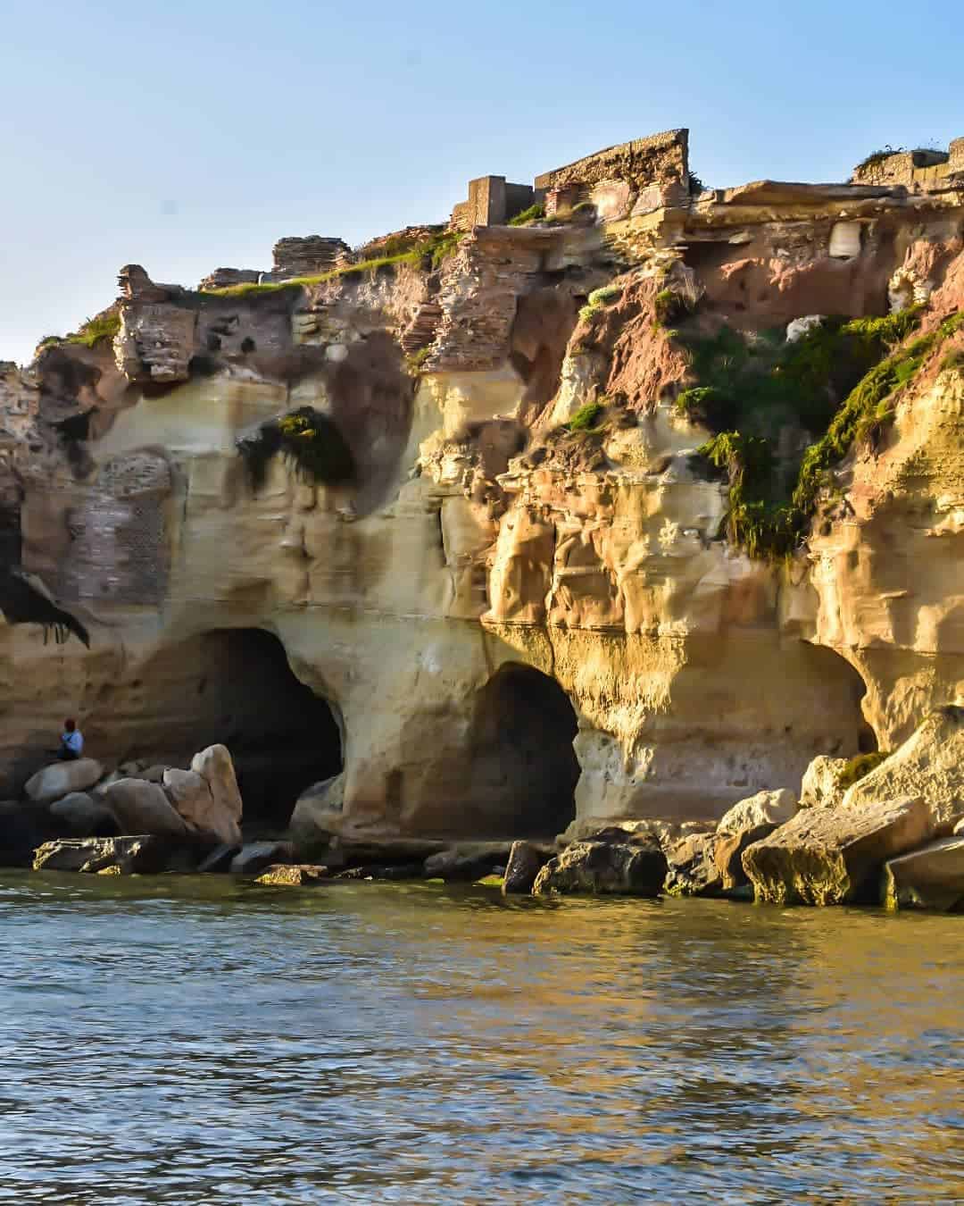 Rocky seaside cliffs with caves and ancient ruins on top, seen in sunlight, with water in the foreground&mdash;one of the best day trips from Rome for families seeking adventure and history.