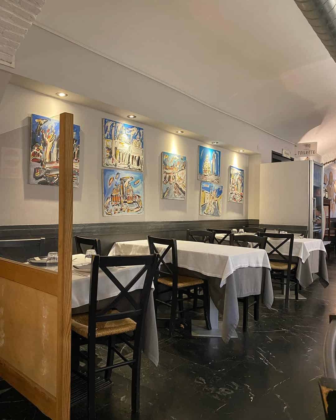 A cozy restaurant with black chairs, white tablecloths, and colorful paintings on the wall—perfect for those seeking Gluten Free Restaurants in Rome.