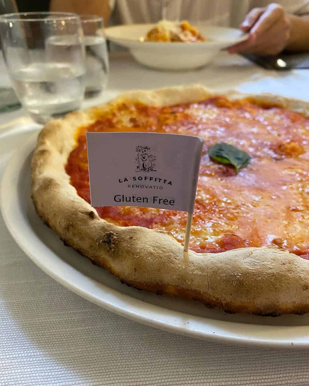 A gluten-free pizza at one of the best Gluten Free Restaurants in Rome, served on a plate with water glasses and a person in the background.