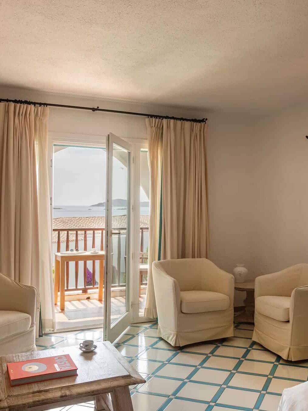 A bright room with two armchairs, a table, and open doors leading to a balcony with a sea view&mdash;perfect for relaxing at one of the best beach resorts in Italy for families.