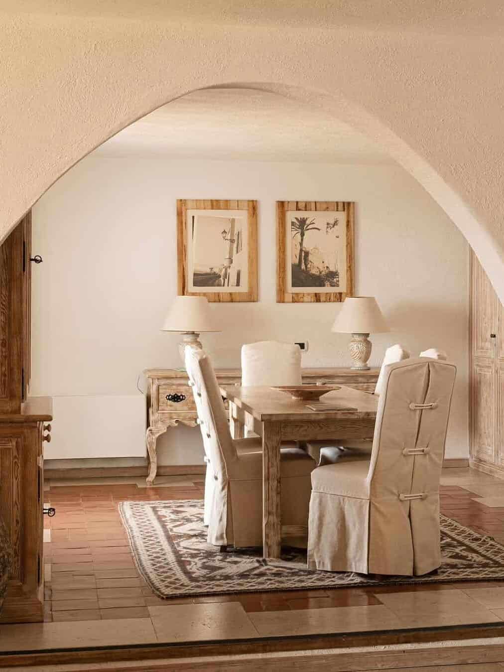 A rustic dining area with a wooden table, cushioned chairs, table lamps, and framed art on the wall&mdash;perfect for gathering after days spent exploring the best beach resorts in Italy for families.