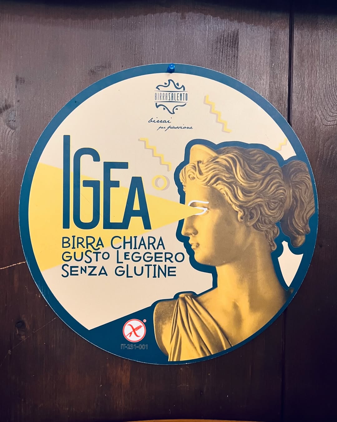 Round sign for IGEA gluten-free light beer, featuring an ancient statue with a yellow geometric design—perfect for those seeking Gluten Free Restaurants in Rome.