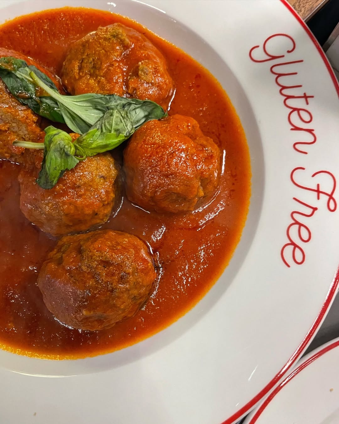 Four meatballs in tomato sauce with basil, served on a plate labeled "Gluten Free" in red script—a perfect dish for those seeking Gluten Free Restaurants in Rome.