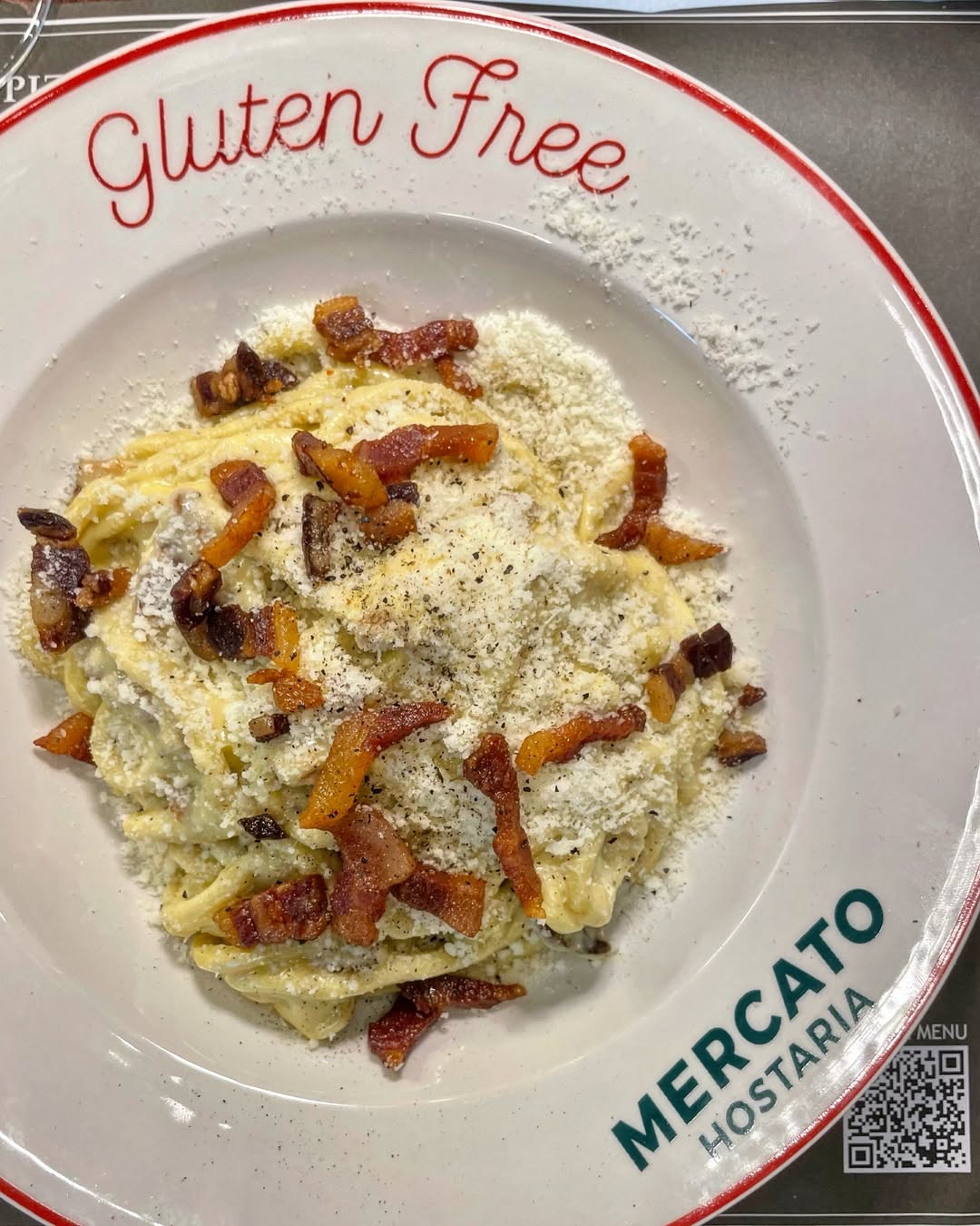 A plate of gluten-free pasta topped with bacon and grated cheese at Mercato Hostaria, one of the top Gluten Free Restaurants in Rome.