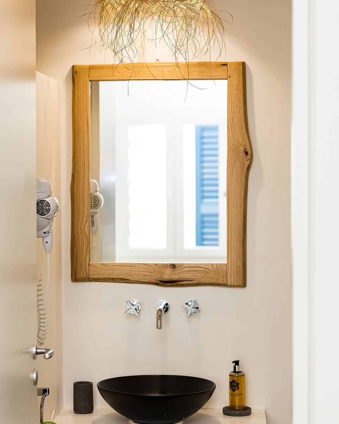 Minimalist bathroom with a wooden-framed mirror, black sink, and wall-mounted faucet below a window&mdash;reminiscent of the serene style found in the best beach resorts in Italy for families.
