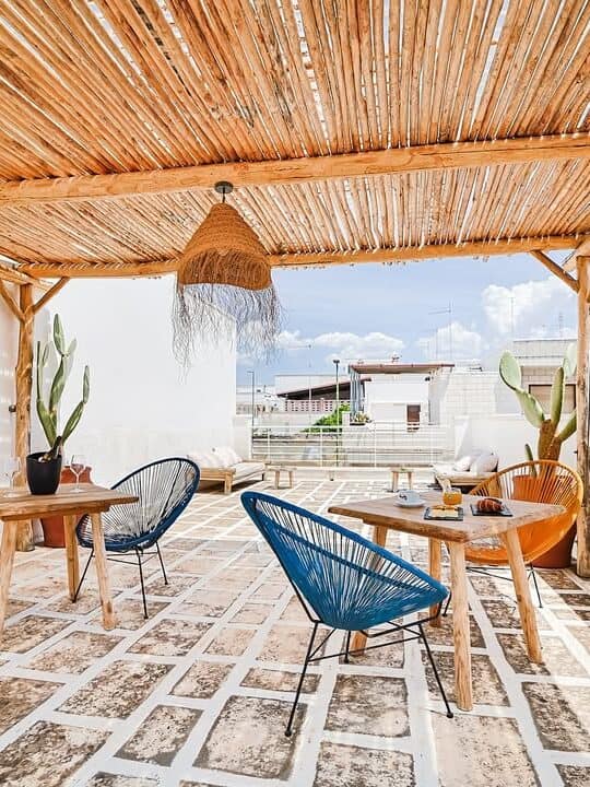 Rooftop patio with wicker chairs, wooden tables, potted cacti, and a bamboo pergola under a blue sky&mdash;reminiscent of relaxing moments at the best beach resorts in Italy for families.