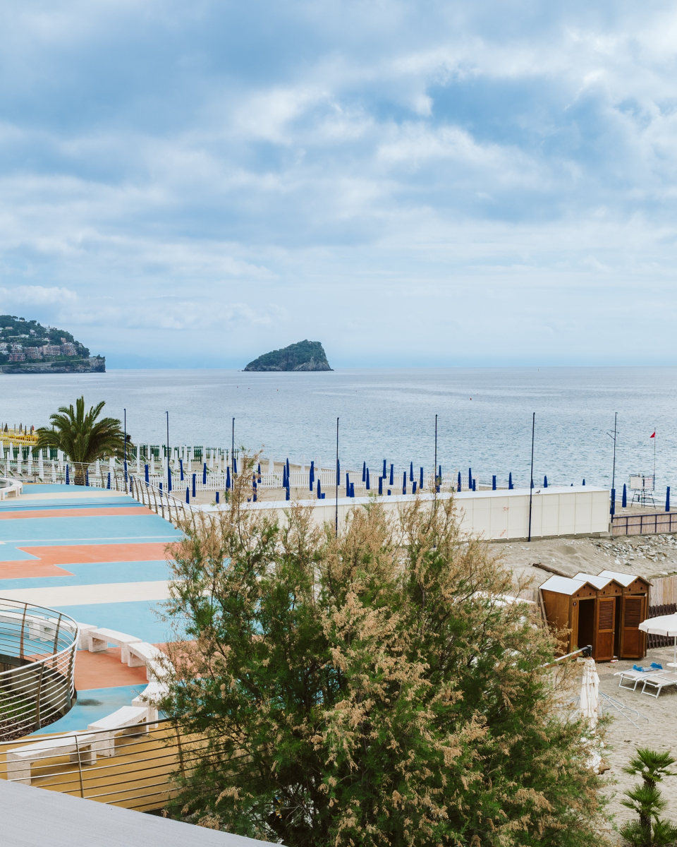 Beach resort with colorful walkways, closed umbrellas, and an island in the distance under a cloudy sky&mdash;one of the best beach resorts in Italy for families.