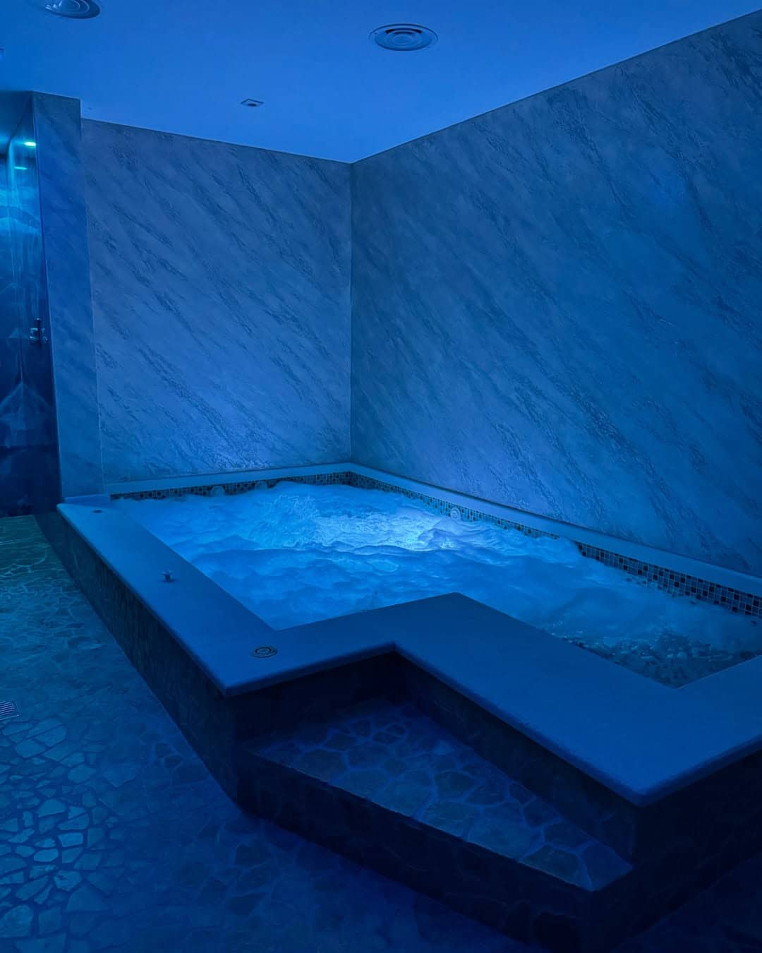 A bubbling jacuzzi tub with blue lighting in a modern, marble-walled spa room&mdash;just like the relaxing amenities found at the best beach resorts in Italy for families.