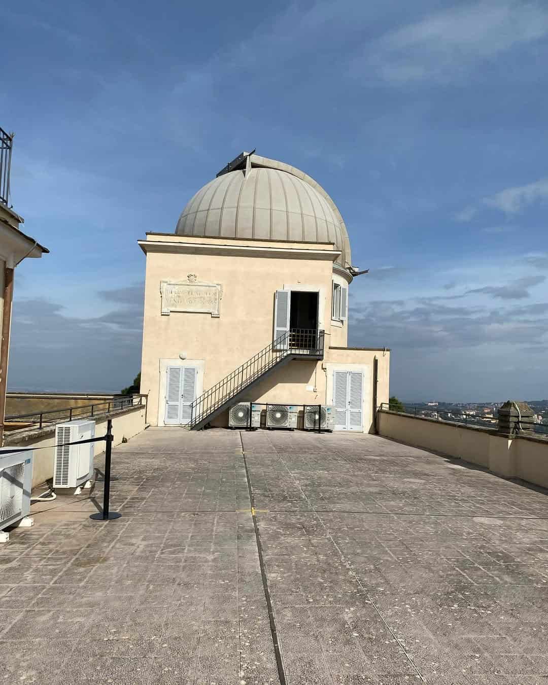 Observatory building with a domed roof and stairs on a rooftop, set under a blue sky with some clouds—a must-see during your 4 days in Castel Gandolfo.