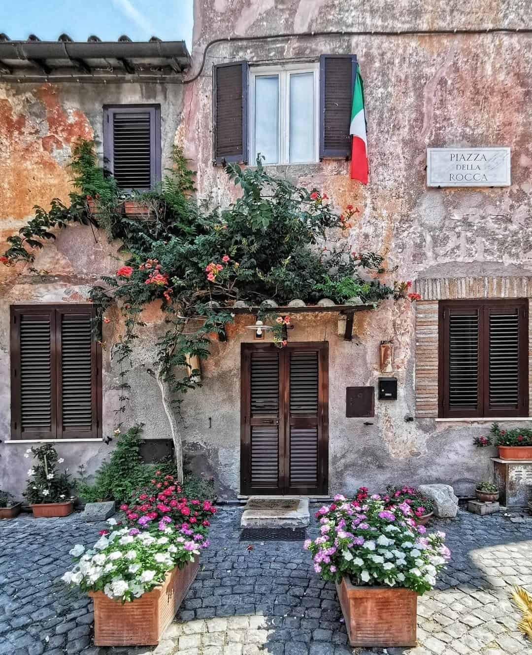 Charming old Italian building with shutters, flowering plants, and an Italian flag on a cobblestone street&mdash;perfect for those seeking the best day trips from Rome for families.
