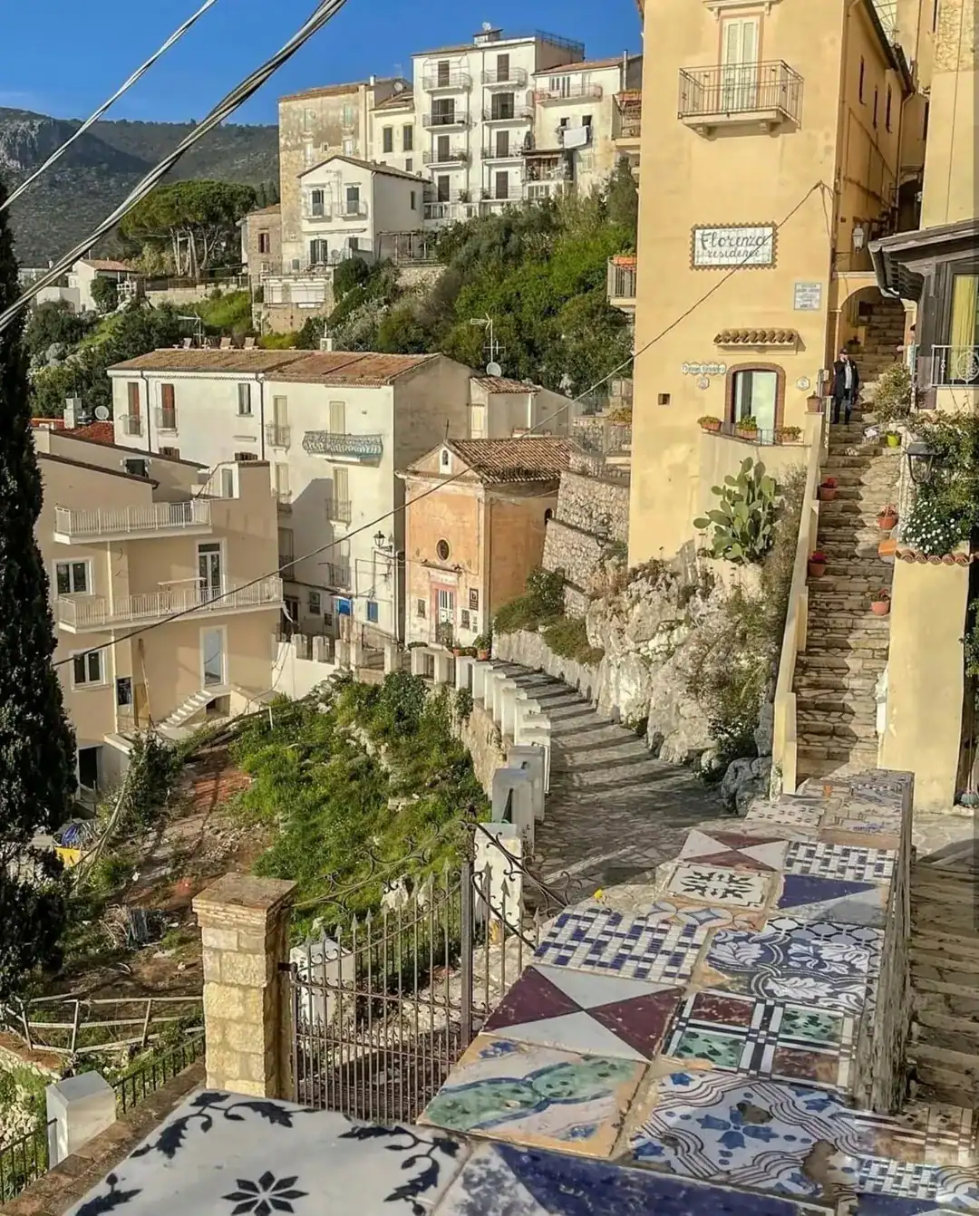 A colorful tiled wall overlooks a charming hillside village with pastel buildings and stone steps in sunlight&mdash;perfect for those seeking the best day trips from Rome for families.
