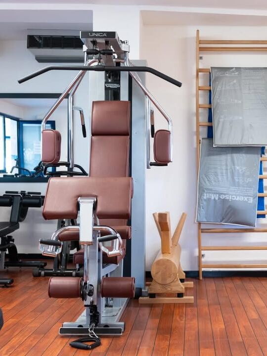 A gym with a weight machine, wooden ladder, exercise mats, and cardio equipment on a wooden floor&mdash;perfect for staying active before relaxing at one of the best beach resorts in Italy for families.