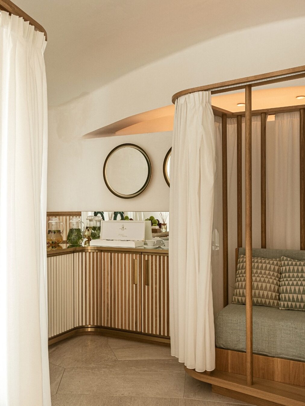 A cozy, modern room with wood accents, round mirrors, a bench with pillows, and white curtains&mdash;perfect for relaxing after exploring the best beach resorts in Italy for families.