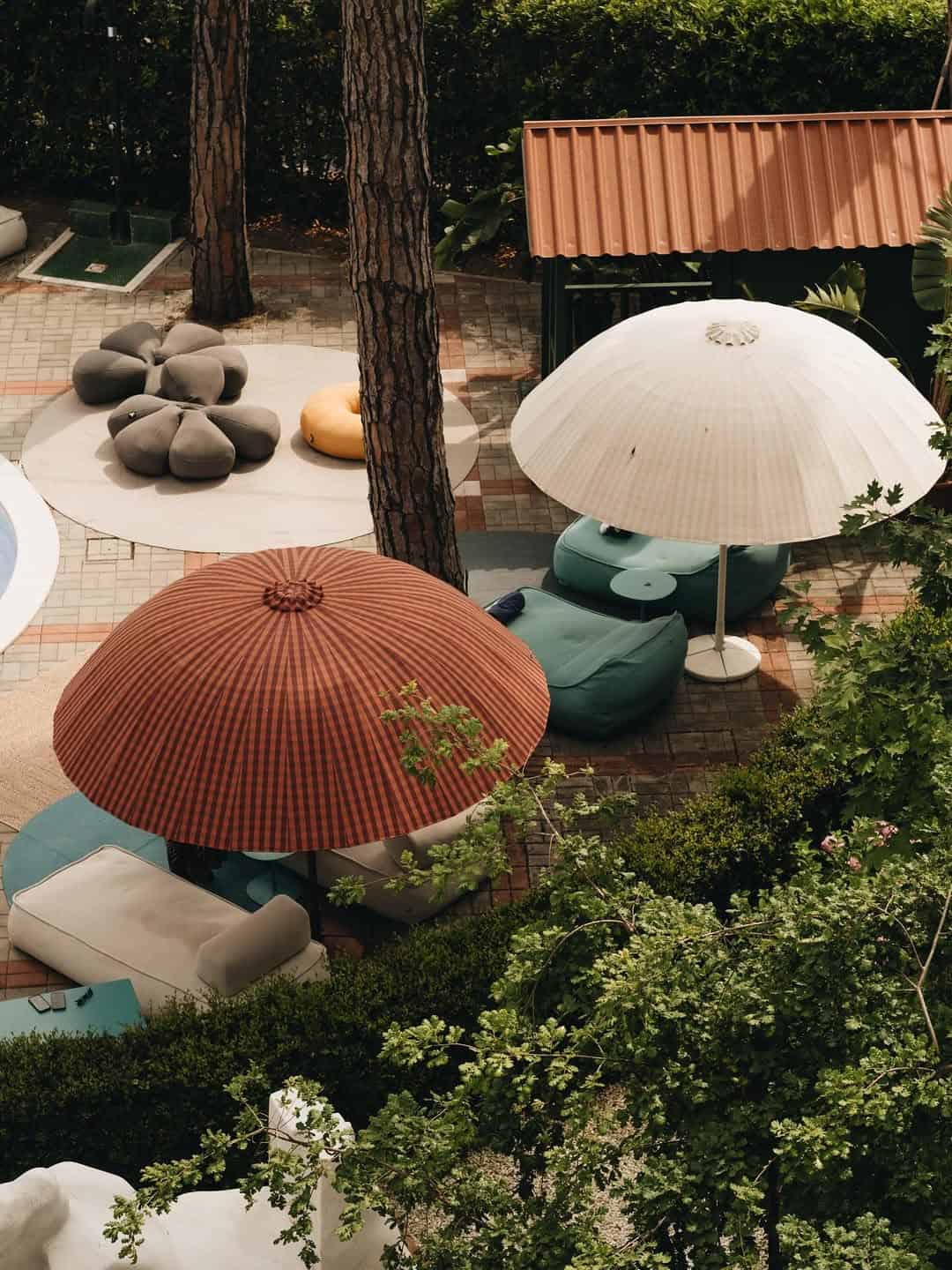 Aerial view of outdoor lounge chairs and two large umbrellas near a pool, surrounded by greenery&mdash;an inviting scene reminiscent of the best beach resorts in Italy for families.