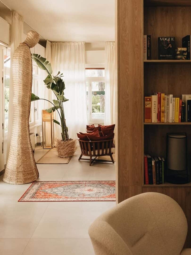 Cozy living room with bookshelves, armchairs, a large woven sculpture, plants, and natural sunlight streaming in&mdash;perfect for relaxing after exploring the best beach resorts in Italy for families.