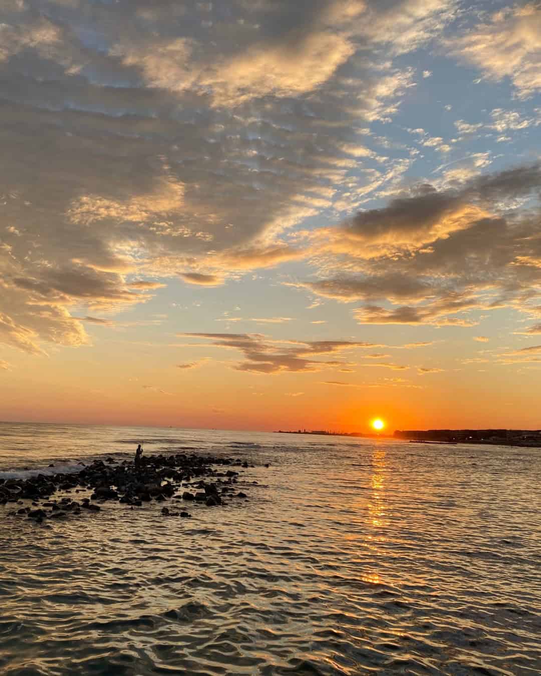 Golden sunset over a calm sea with clouds and rocks in the foreground, capturing the tranquil beauty often found on the best day trips from Rome for families.