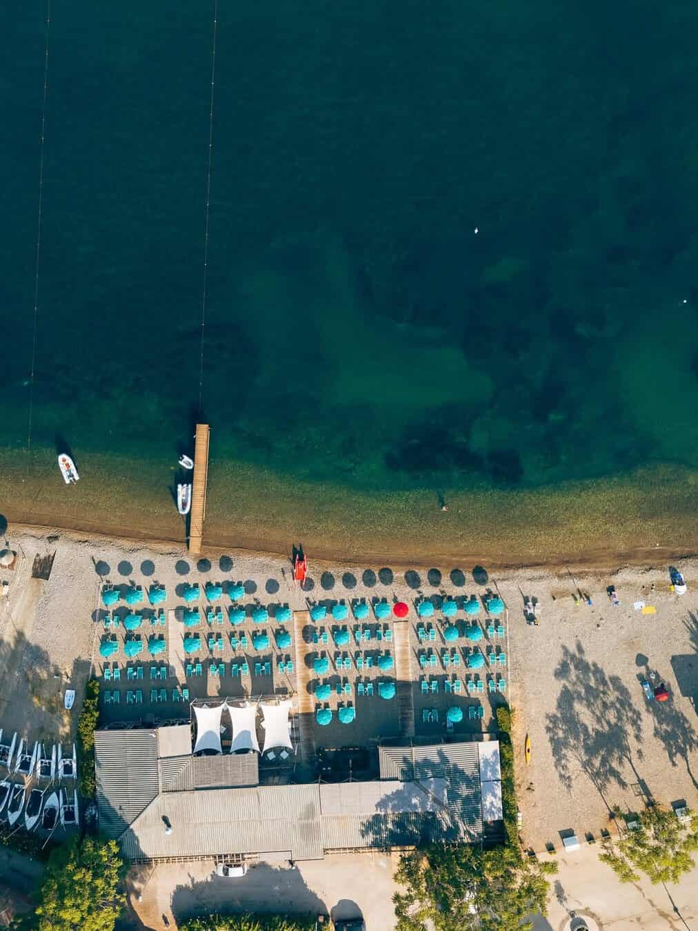 Aerial view of one of the best beach resorts in Italy for families, with rows of turquoise umbrellas, sunbeds, and clear blue-green water.