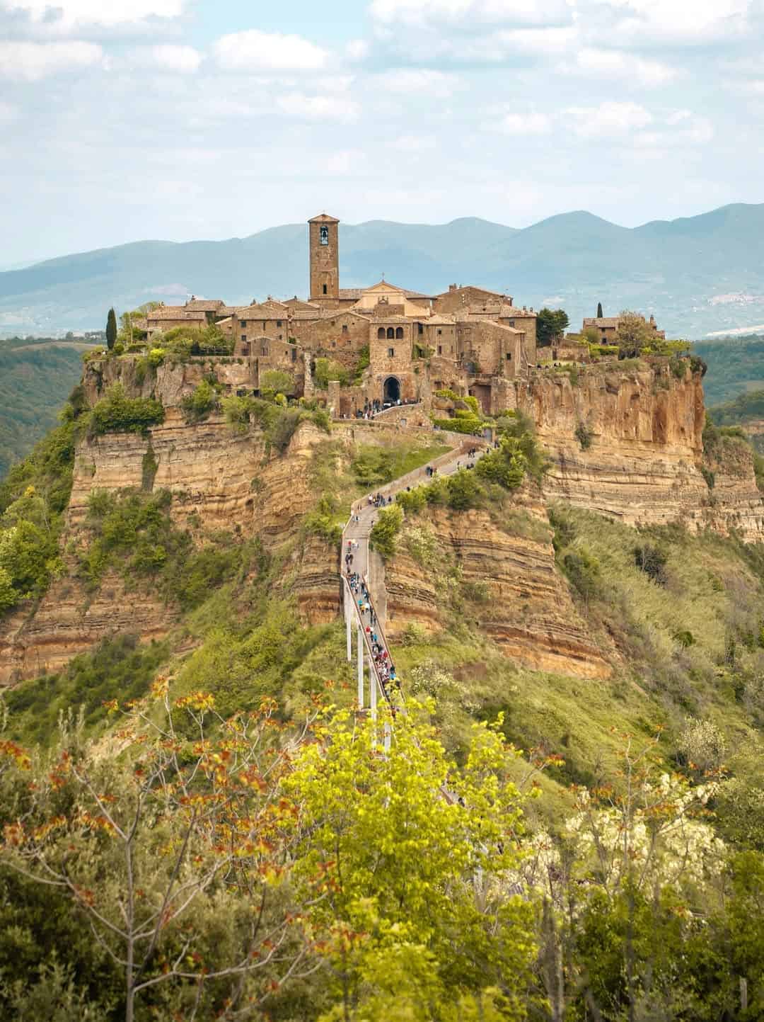 Hilltop medieval village with a stone bridge, surrounded by cliffs and greenery, mountains in the background&mdash;one of the best day trips from Rome for families seeking scenic history and adventure.