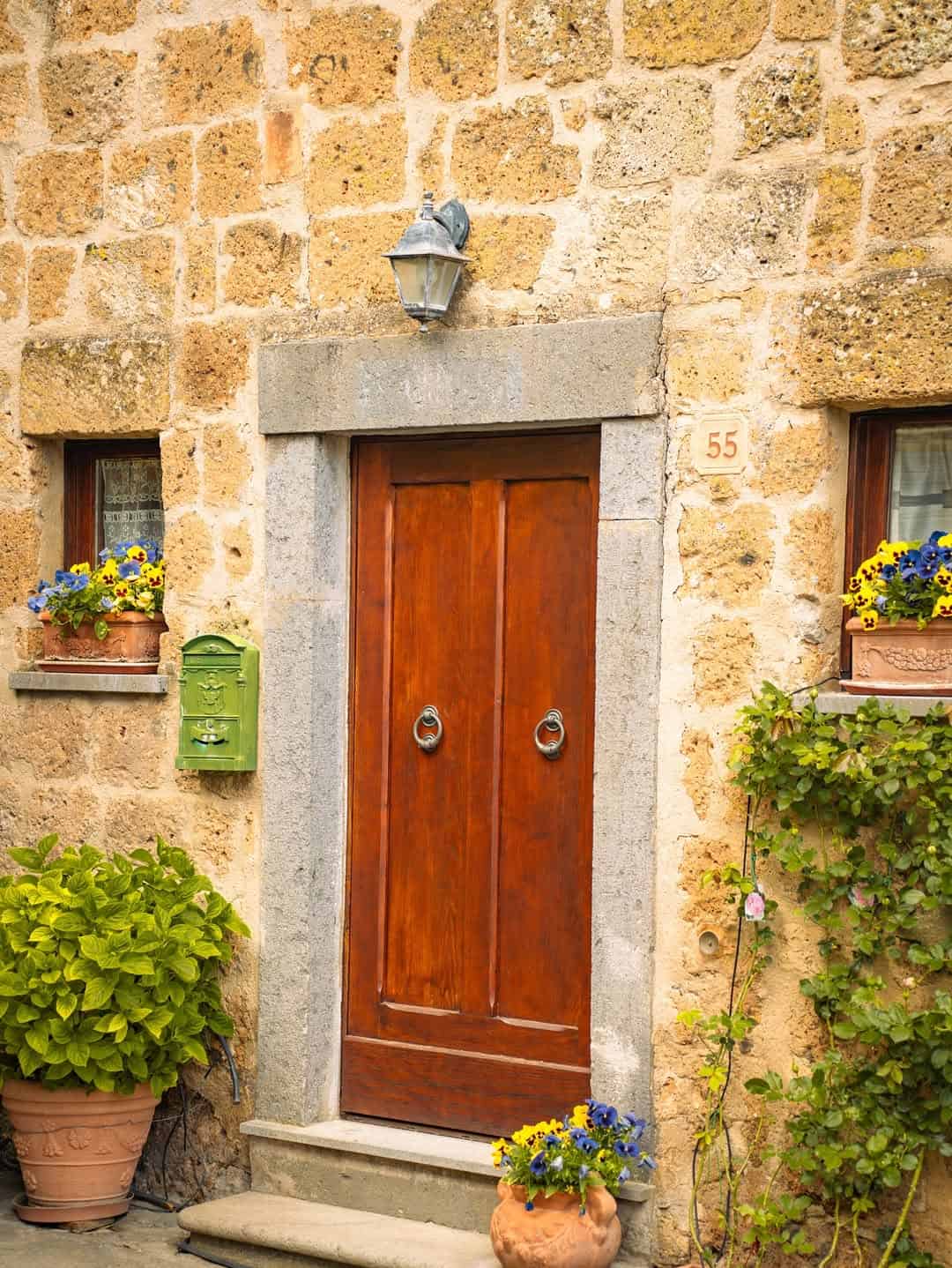 A charming wooden door in a stone wall, flanked by flower-filled windows, a green mailbox, and potted plants&mdash;perfect for inspiring memories of the best day trips from Rome for families.