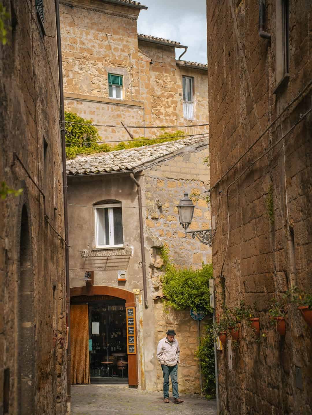 Man in hat walks down a narrow, rustic stone alley lined with plants in an old European town&mdash;one of the best day trips from Rome for families seeking charm and adventure.