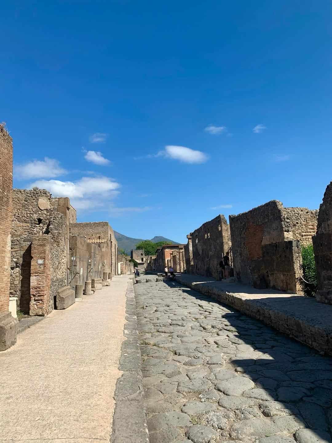 Ancient stone street and ruins of Pompeii under a clear blue sky with scattered clouds&mdash;a fascinating site often included in the best day trips from Rome for families.
