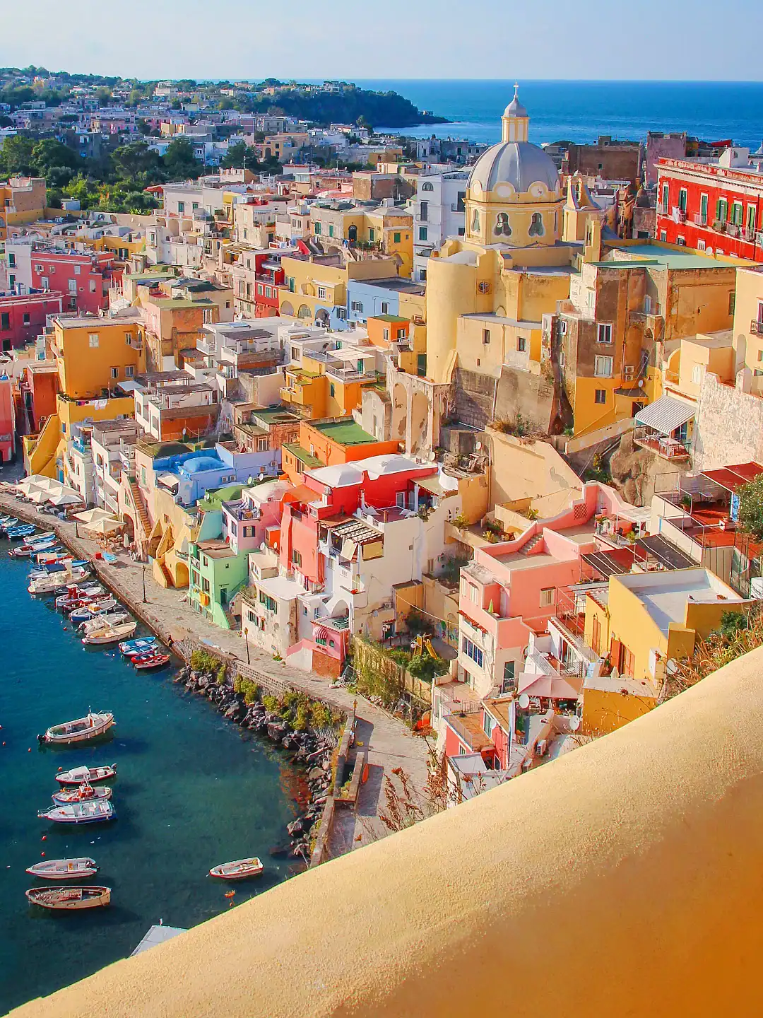 Colorful buildings and boats line this charming coastal town&mdash;one of the best day trips from Rome for families&mdash;with a domed church, blue sea, and green hills painting a stunning backdrop.