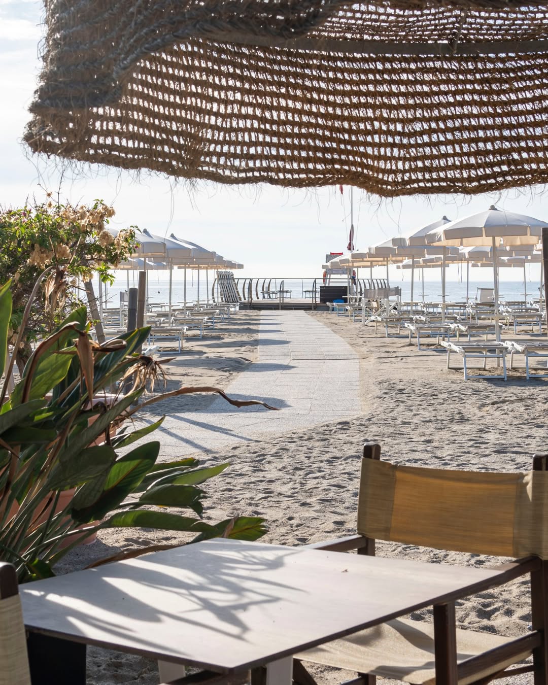 A sunny beach scene with empty lounge chairs, umbrellas, and a shaded table in the foreground&mdash;just like you&rsquo;d find at the best beach resorts in Italy for families.