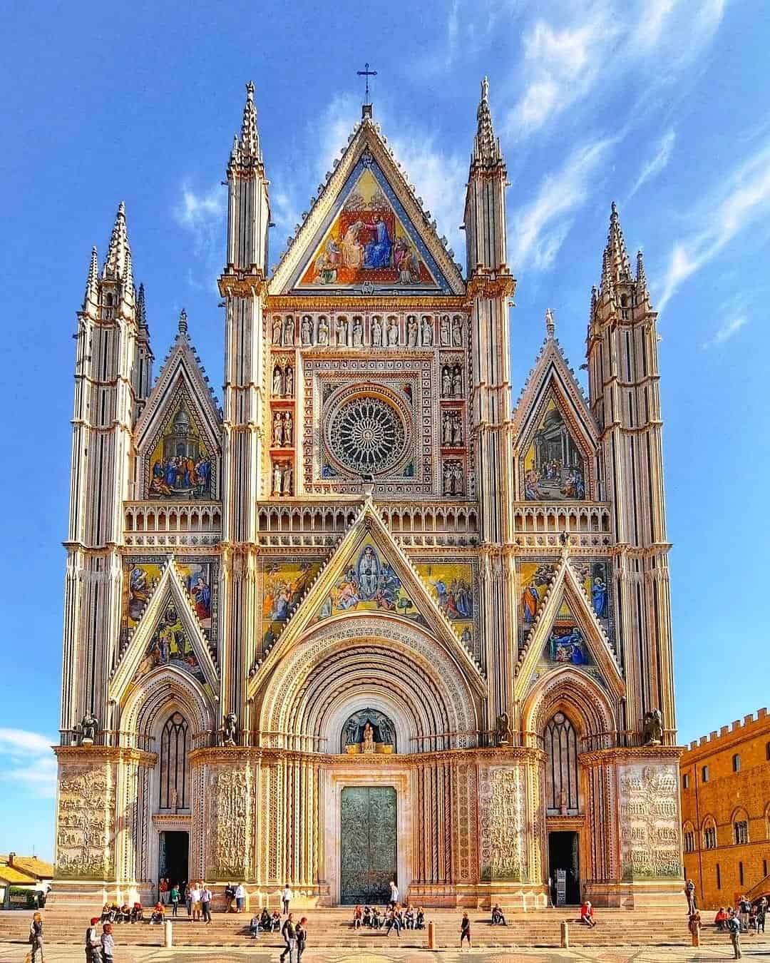 Colorful facade of Orvieto Cathedral with intricate mosaics, rose window, and spires under a blue sky&mdash;one of the best day trips from Rome for families to experience art and history together.