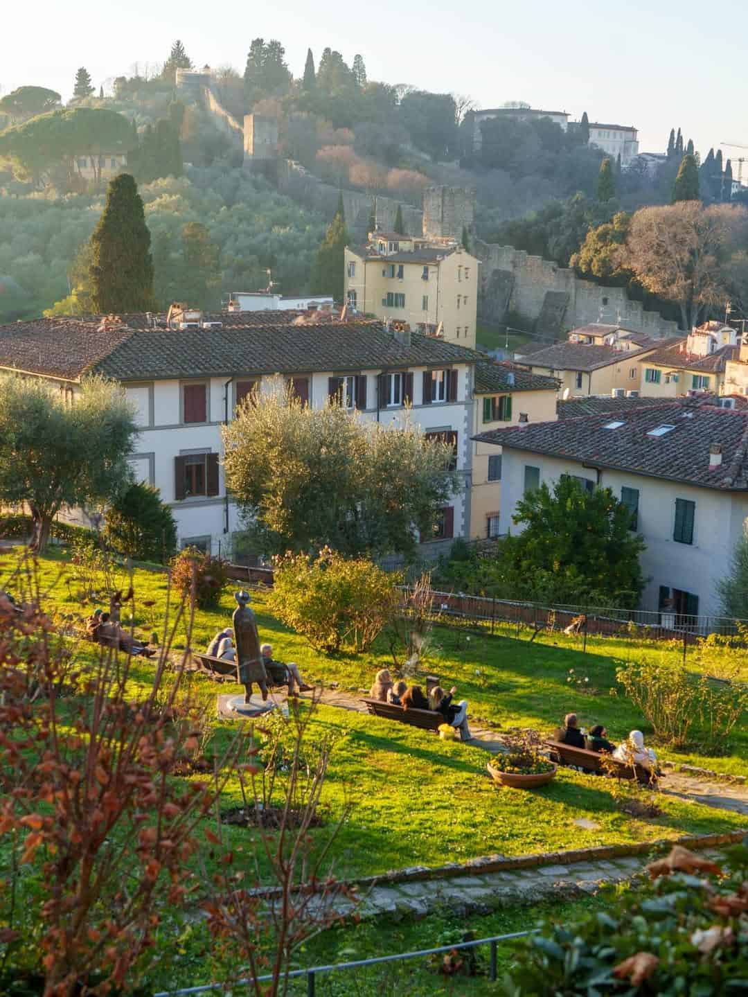 People relaxing on benches in a sunny garden with houses and a hillside in the background&mdash;an ideal scene that could be found on one of the best day trips from Rome for families.